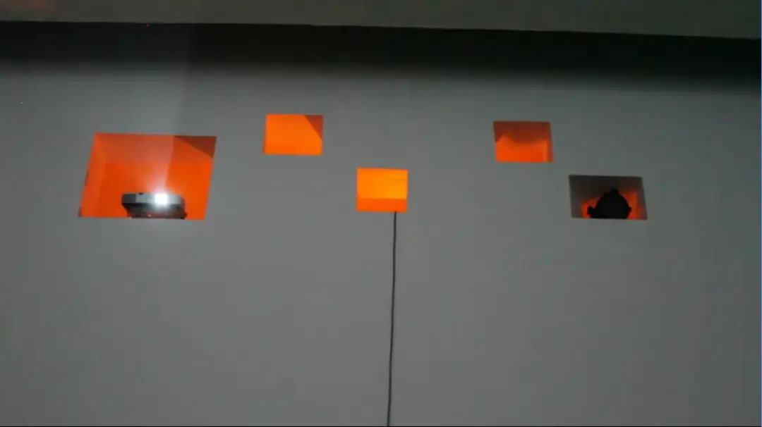 A low lit wall with holes in the wall and a cable coming out of a hole down the wall.