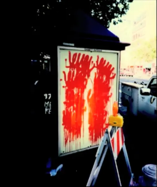 a messy graffitied poster with dripping unreadable tags, and a construction barrier in front