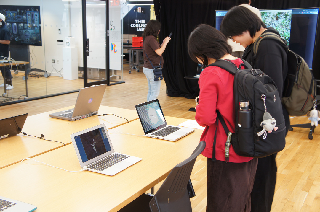 2 students look at older laptop showing artwork on screen