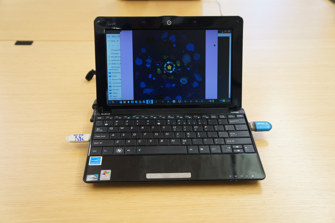 an old Eee PC laptop with 2 USB sticks and a screen showing circular artwork of sea life