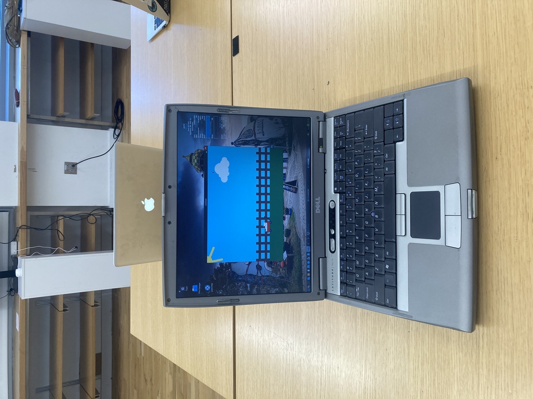 a very old Dell Latitude laptop from 2005 displaying a project coded in L5 showing a kitty in a cart in front of a picket fence and sun and clouds