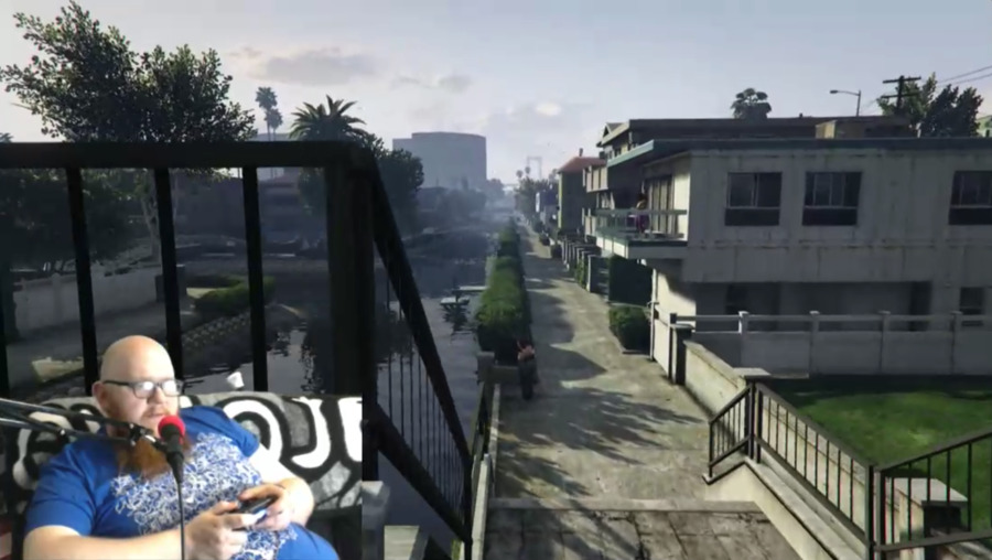 Screenshot of man in lower left on top of game screen from Grand Theft Auto V showing an overlook down to some apartments