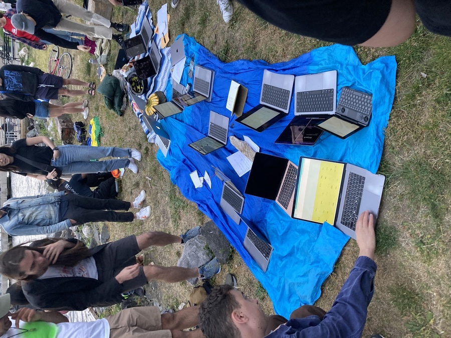 A blue blanket with laptops and notebooks piled up all around and people standing around them