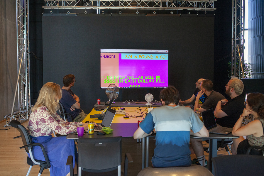 A group of people in a workshop sitting around a larger monitor screen showing a bright punk website